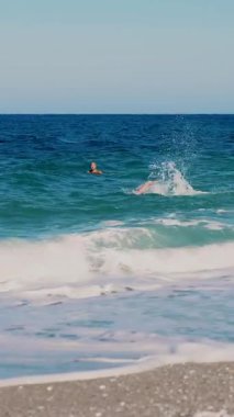 Turkuazda, denizin mavi sularında, iki adam yüzer. Yaz sıcağı güneşli bir gün. Denizde yumuşak dalgalar, sahilde. Beyaz köpüklü dalgalar kıyıya vurur..