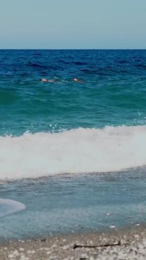 Turkuazda, denizin mavi sularında, iki adam yüzer. Yaz sıcağı güneşli bir gün. Denizde yumuşak dalgalar, sahilde. Beyaz köpüklü dalgalar kıyıya vurur..