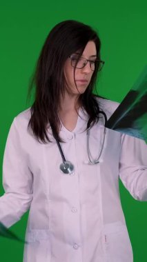 Gözlüklü, beyaz tıbbi üniformalı ve steteskoplu kadın doktor portresi yeşil arka plandaki hastaların akciğerlerinin röntgen görüntülerini inceliyor..