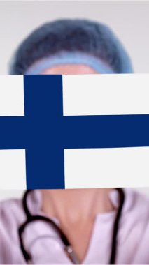 Yakın plan. Gözlüklü doktor, mavi tıbbi şapkalı, eldivenli Finlandiya bayrağıyla el maskesi takıyor. Doktorlar, koronavirüs sırasında devletin koruması, küresel salgın. Kavram