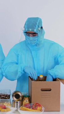 Koruyucu eldivenler içinde gönüllü, market alışverişini karton bağış kutusuna paketliyor. Coronavirus sırasında paket servis, kapı yemek servisi. İnternetten alışveriş. Hayırseverlik.