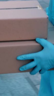 Yakın plan, Coronavirus salgını sırasında hastaneye tıbbi ekipman ya da uyuşturucu taşıyan paket teslimatı. Kurye, koruyucu kıyafetli, hemşireye karton kutular veriyor. Kargo teslimat servisi karantina sırasında.