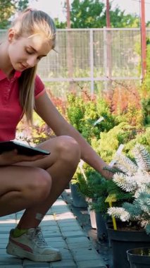 Kadın bahçıvan bitkilerin kalitesini kontrol eder, dijital tablete not alır, bahçe merkezi ya da sera boyunca yürür. Bitkileri büyütmek ve onlarla ilgilenmek. Çiçekçilik, bahçıvanlık, bahçıvanlık, çiçek işi..