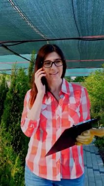Kadın bahçıvan ya da çiçekçi telefonla konuşuyor, elinde dijital tablet var, bahçe merkezinde ya da serada. Bitkileri büyütmek ve onlarla ilgilenmek. Çiçekçilik, bahçıvanlık, bahçıvanlık, çiçek işi..