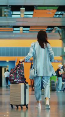 Havaalanı koridorunda bavuluyla yürüyen maskeli kadın hava yolcusu kalabalığının arka planında. Kalkışı bekliyor. Coronavirüs salgınından sonra seyahat.