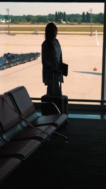 Elinde bavul ve dizüstü bilgisayarla iş kadınının karanlık silueti havaalanının vergisiz bekleme odasının geniş penceresine doğru yürüyor..