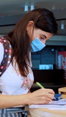 Koruyucu maskeli bir kadın, elinde pasaport ve biletler var, belgeleri dolduruyor, havaalanında tıbbi anket dolduruyor. Coronavirüs salgınından sonra yeni kurallar ve kısıtlamalar. Uçuşların devamı, açık sınırlar