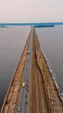 Hava görüntüsü. Nehrin karşısında, trafiği aktif olan bir baraj. Küçük bir motosiklet sütunu, yol boyunca bisiklet sürüşleri.