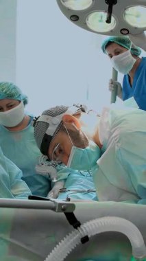 Tıbbi maske takan ve özel lensler takan bir cerrah, asistanıyla birlikte hastane ameliyathanesinde ameliyat yapıyor. ameliyat, resüsitasyon veya yoğun bakım.