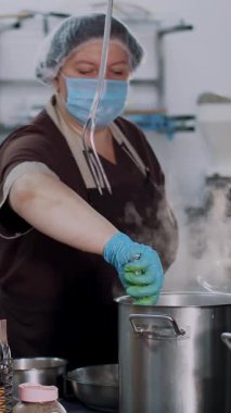 Yemek pişirmek. Kadın şef, koruyucu eldivenler ve maske takmış, mutfakta yemek hazırlıyor, kantinde. Sağlıklı gıda ve güvenlik kavramı. Matarayı yeniden aç