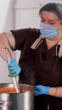 Yemek pişirmek. Kadın şef, koruyucu eldiven ve maske takıyor, mutfakta yemek hazırlıyor, kantinde. Sağlıklı yemek. Güvenlik kavramı. Matarayı yeniden açıyorum. Gönüllülük ve yardım