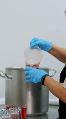 Yemek pişirmek. Yakın plan. Yemek pişirir, koruyucu eldiven takar ve maske takar, demlenmiş meyve suyu döker, büyük demlikten bardaklara meyve suyu döker. Sağlıklı yemek. Gönüllü olmak ve yardım. Yeniden açılıyor. güvenlik kavramı.