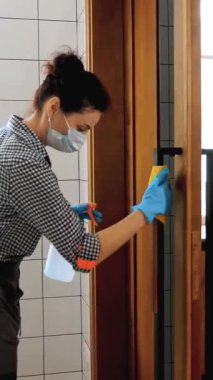 Bayan temizlikçi, koruyucu maskeli ve eldivenli, restoranda ya da kamu kuruluşunda antiseptikle kapı kollarını siliyor. Koronavirüse karşı koruma, güvenlik kavramı