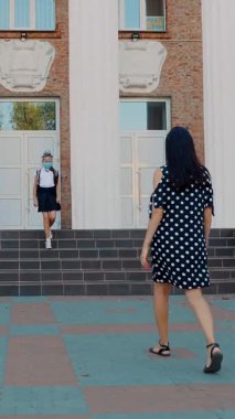 Anne okul bahçesinde kızıyla tanışır. Okul kızı ve kadın, ikisi de koruyucu maskeler takıyor. 19. salgından sonra okula döndüm. Covid-19 saatinde selamlar.