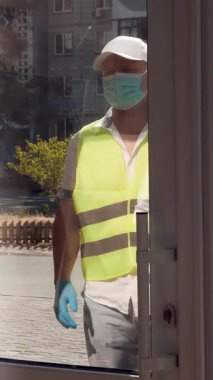 Paketler için teslimat hizmeti, hediyeler. Kurye koruyucu maske takıyor. Tasarımcı, maskeli, hediye çantası takıyor. Koronavirüs salgını yüzünden eve servis. Online satış, online alışveriş.