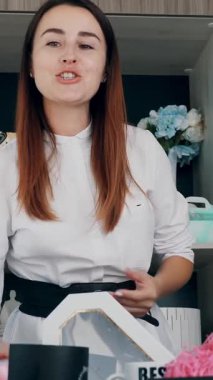 Tasarımcı hediye paketliyor. Çekici kadın dekoratör online yayın, konferans, video blogu, web sitesi, akıllı telefonun önünde duruyor. çevrimiçi çalış.