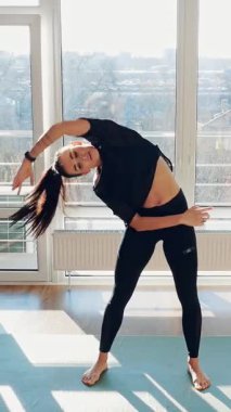 Bayan fitness koçu akıllı telefon kullanarak online egzersiz gösteriyor. Tecrit sırasında zindelik. Evde spor yapan genç bir kadın. Zindelik, sağlık ve sağlıklı yaşam tarzı kavramı