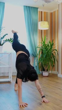 Çevrimiçi antrenman, uzaktan. Spor giyim bölümünde, spor salonunda spor koçuyla özel ders videosu seyreden ve evde egzersiz yapan genç bir kadın. Kilit altında spor yaparken, evde.