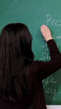 Çevrimiçi eğitim. Öğretmen çevrimiçi İngilizce dersi sırasında materyalleri açıklıyor. Okulda, tahtaya tebeşirle dil bilgisi kuralları yazıyor. Uzaktan eğitim. Sınıftan canlı video yayını.