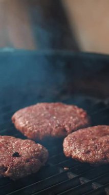 Aşçılık. Hamburger pişirmek. Yakın plan. Restoranın mutfağında, Brezilya usulü, sıcak barbekü ızgarasında hamburgerler için taze et pirzolası pişirme işlemi. Fast food, abur cubur