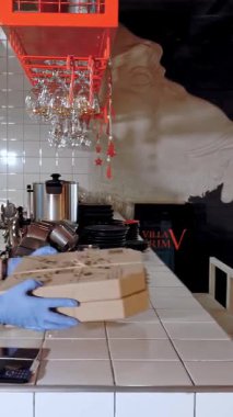 Paket yemek, pizza teslimatı, yemek teslimatı. Koruyucu maskeli genç bir adam pizzacıda pizza kutularına koyar. Coronavirus, tecrit..