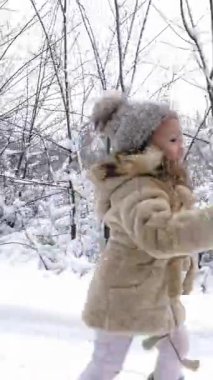 Kış aile aktiviteleri açık havada. Yan görünüş. Mutlu küçük kız yoğun karlar içinde annesine giden yolda koşuyor, kar yağışı sırasında. Aile eğleniyor, karlı kış gününde birlikte vakit geçiriyorlar.