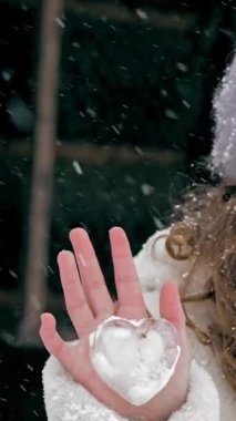 Kış portresi. Sevimli, güzel küçük kız, kar taneleriyle kaplı, el ele tutuşmuş, kar yağarken, buzdan ev yapımı Noel ağacı oyuncağı. Ahşap evin arka planı. Karlı kış gününde mutlu günler..