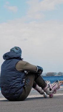 Dışarıda paten kayarken. Dışarıda paten kaymak. Kaygısız adam, tekerlekli sandalyede kumlu plajın yanında güneşli bahar günlerinde deniz manzarasına hayran bir şekilde dinleniyor..