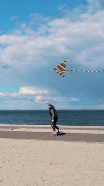 Uçurtma. Dışarıda paten kayarken. Kaygısız adam uçurtma uçuruyor, plaj boyunca paten kayarken, ılık bir bahar gününde açık havada. Mutlu adam hafta sonu dışarıda eğleniyor.