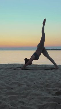 Açık havada uzanıyor. Yoga silueti. Yoga kumsalı. Atletik genç kadın gün batımında ya da gün doğumunda plajda yoga yapıyor. Spor salonu açık havada. Sabahları spor yapıyorum..