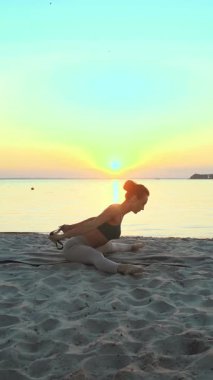 Açık havada uzanıyor. Fitness elastik bant. Atletik genç kadın gün batımında veya gün doğumunda plajda spor yaparken elastik bant kullanıyor. Spor salonu açık havada..