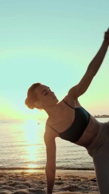 Barda idman. Açık havada uzanıyor. Yoga kumsalı. Atletik genç kadın gün batımında ya da gün doğumunda plajda minder üzerinde egzersiz yapıyor. Spor salonu açık havada. Fitness, bale, spor, yoga