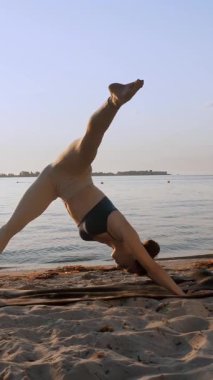 Barda idman. Açık havada uzanıyor. Yoga kumsalı. Atletik genç kadın gün batımında ya da gün doğumunda plajda minder üzerinde egzersiz yapıyor. Spor salonu açık havada. Fitness, bale, spor, yoga