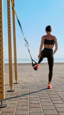 Açık havada egzersiz. Askı kayışları. Kayışlarla egzersiz yap. Atletik genç kadın gün batımında veya gün doğumunda plajda halatla tüm vücut direnci egzersizleri yapıyor..