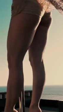 Direk dansı. uygun kadın jimnastikçi, bej mayosuyla, akrobatik egzersizler yapıyor metal döner direkte, gökdelen çatısında, muhteşem bir gündoğumu görüşü arka planında