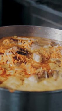 Yemek pişirmek. Güveç. Açık büfe restoran mutfağı. Yakın plan. Yemek buharlaşıyor, tencerede kaynıyor. Ticari bir mutfakta yemek hazırlamak ve pişirmek.