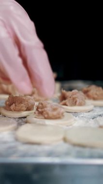 Yarı bitmiş ürünler. Yemek pişirmek. Yakın plan. Aşçının elleri hamur, mantı, ravioli ve pelmeni yapmak için hamur üzerine doğranmış et parçaları serer. Açık büfe restoran mutfağı..