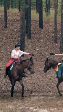İgbt. Gökkuşağı. Aynı cinsiyette aşk. Lezbiyen kadınların genç çifti ortak bir hobiyle meşgul, ata biniyorlar. Kız arkadaşlar ormanda at biniyor, eğleniyorlar.
