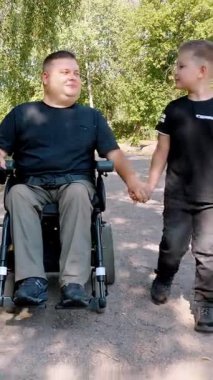 Engelli biri. Baba ve oğul. Babalar Günü. Baba ve küçük tatlı oğlu bir yaz günü parkta yürüyorlar. Babam tekerlekli sandalye kullanıcısı..