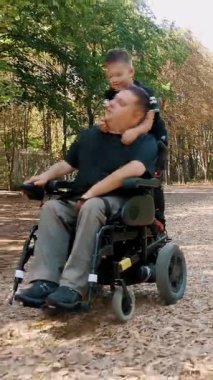 Engelli biri. Baba ve oğul. Babalar Günü. Baba ve küçük tatlı oğlu bir yaz günü parkta yürüyorlar. Babam tekerlekli sandalye kullanıcısı..