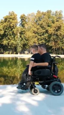 Baba ve oğul. Babalar Günü. Baba ve küçük oğlu bir yaz günü bir göletin yanındaki parkta yürüyorlar. Babam tekerlekli sandalye kullanıcısı. Çocuk babasının kucağında oturuyor..