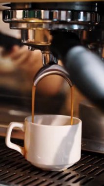 Kahve içeceğim. Yakın plan. Kahveci kahve makinesini kullanarak kahve hazırlar. İnce kahve akıntısı espresso makinesinden küçük beyaz bir fincana akar..