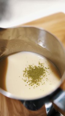Kibrit. Matcha Green tea latte içeceği. Yakın plan. Kuru yeşil kibrit tozu sütle sürahiye dökülür. Sıcak süt içeceği ve kibrit yeşili çay hazırlamak için.