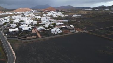 wide orbit overview drone Village with white houses in black lava field from volcanic ash, Lanzarote Canary Islands Spain, cloudy day 2023. High Quality 4k Cinematic footage.