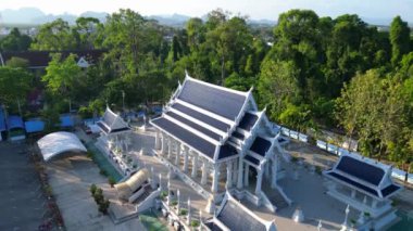 Yukarıdan aşağıya insansız hava aracı. Arka planda tropik manzarası olan sakin bir Tayland tapınağının üstünden geçiyor.