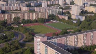 Kentsel spor kompleksi ve yerleşim alanı. Panorama yörünge dronu. Kalabalık bir şehrin yüksek binalarının ortasındaki bir spor sahasının kuş bakışı görüntüsü.