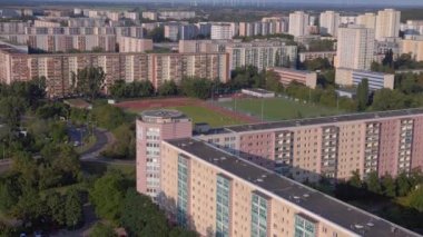 Kentsel spor kompleksi ve yerleşim alanı. İHA iniyor. Kalabalık bir şehrin yüksek binalarının ortasındaki bir spor sahasının kuş bakışı görüntüsü.