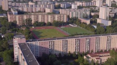 Kentsel spor kompleksi ve yerleşim alanı. Panorama yörünge dronu. Kalabalık bir şehrin yüksek binalarının ortasındaki bir spor sahasının kuş bakışı görüntüsü.