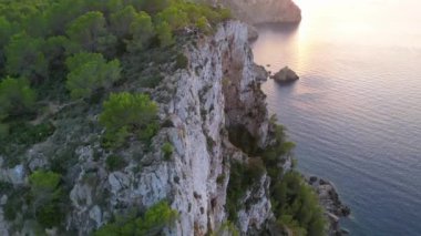 Ufuktaki günbatımının panoramik görüntüsü kayalık bir deniz uçurumuna ve sakin bir okyanusa bakıyor. Yüksek kalite 4k görüntü