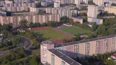 Kentsel spor kompleksi ve yerleşim alanı. İHA iniyor. Kalabalık bir şehrin yüksek binalarının ortasındaki bir spor sahasının kuş bakışı görüntüsü.